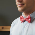 Man wearing a white shirt with a red Valentines Day bow tie featuring white heart patterns against a dark background