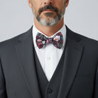 Man wearing a Cabernet floral bowtie and black suit with a white shirt on a light gray background