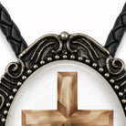 a close-up view of a decorative cross pendant with intricate metalwork and a wooden cross at its center.