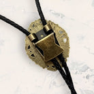 A close-up view of a decorative metal piece with a black braided cord attached to it.