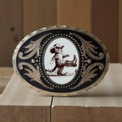 Decorative belt buckle with a cat in cowboy attire on a wooden surface