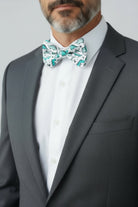 Man wearing a gray suit with a white shirt and a dinosaur bow tie against a light gray background