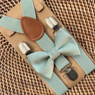 Sage bow tie and Sage suspenders set on a woven surface