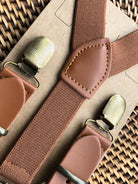 Wedding suspenders for groomsmen with bronze clips on a woven surface