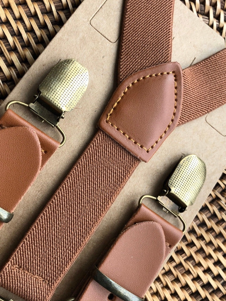 Wedding suspenders for groomsmen with bronze clips on a woven surface