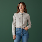 Woman wearing a beige shirt and blue jeans and a raven bolo tie against a green background