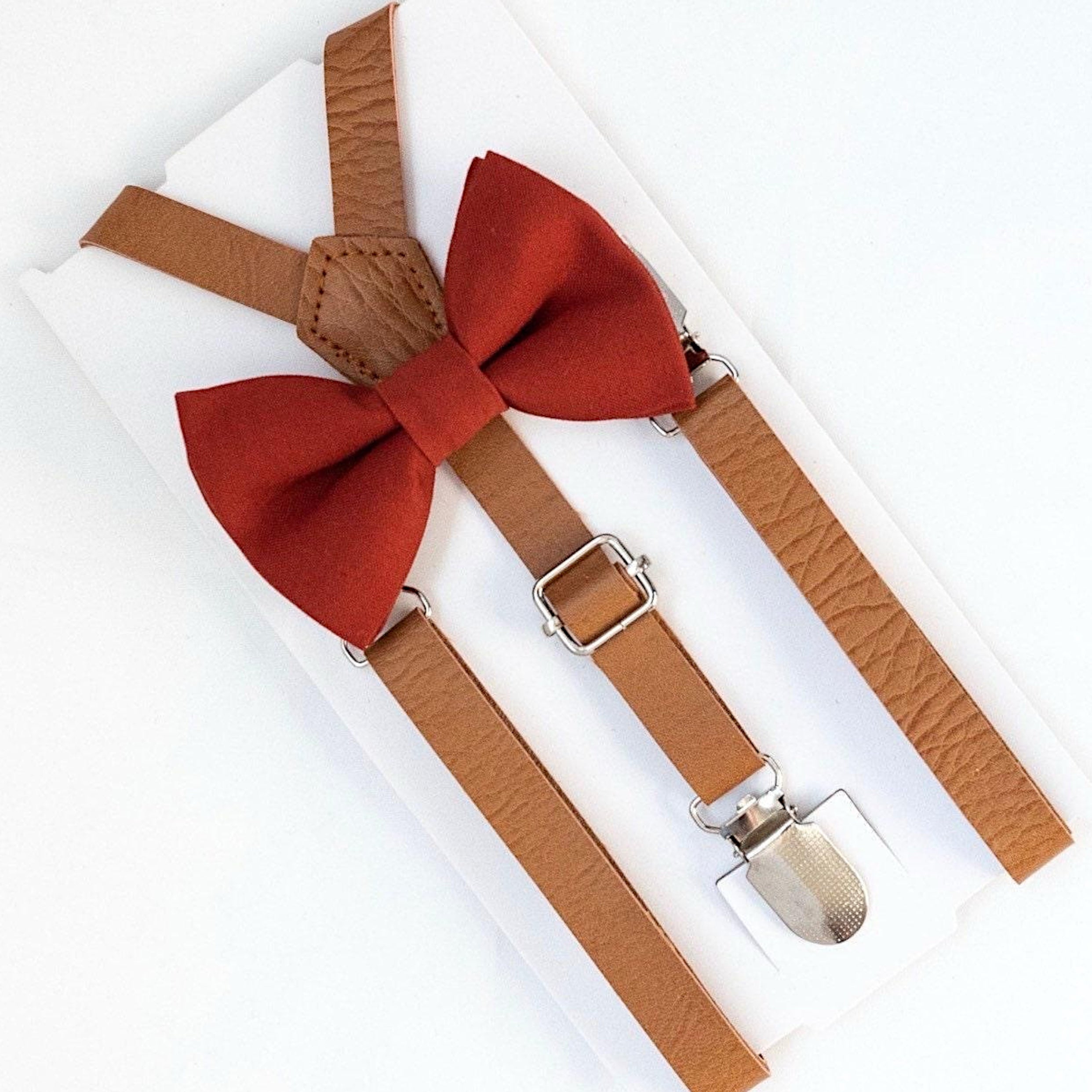 Burnt orange bow tie and brown suspenders on a white background