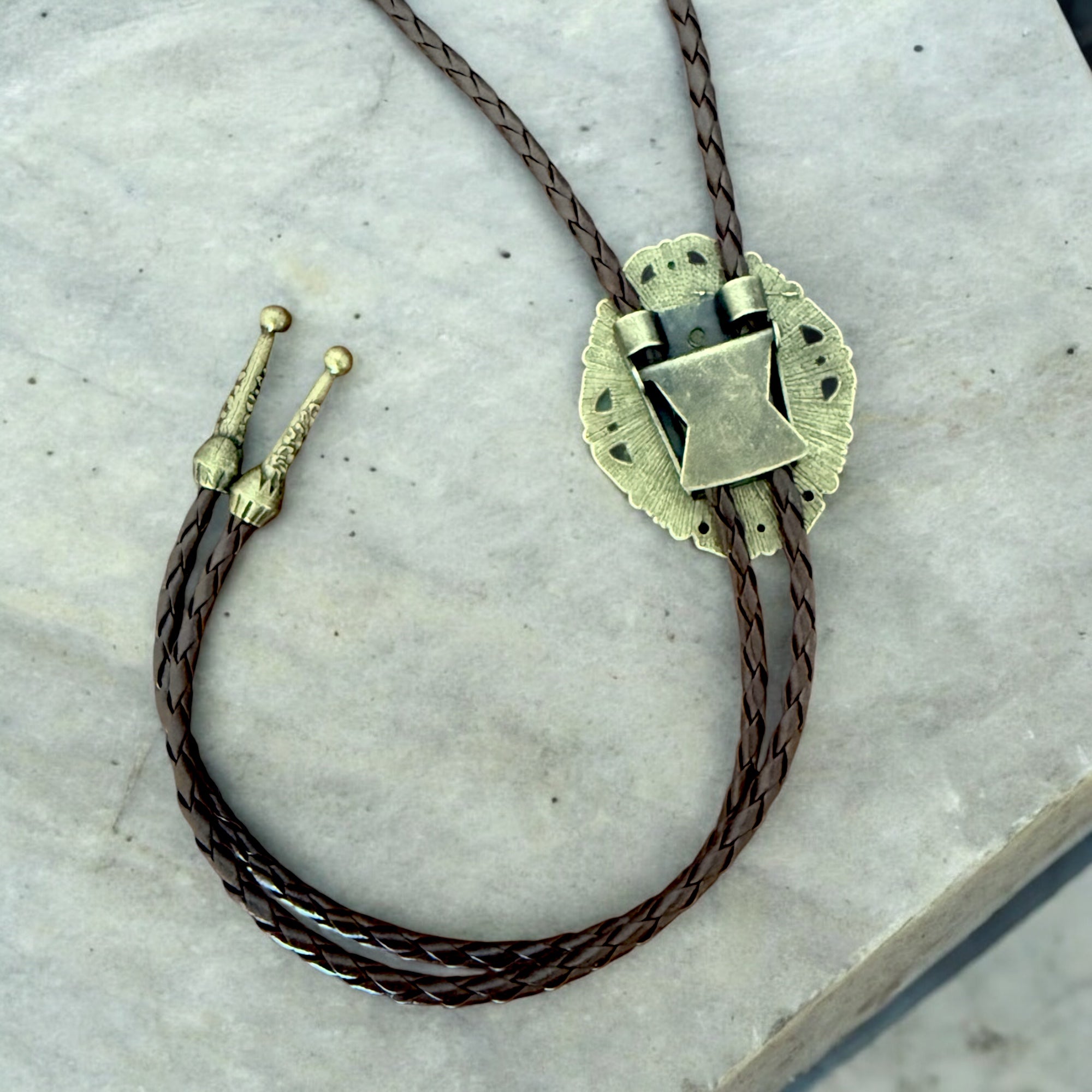 Bolo tie with bronze clasp on a marble surface