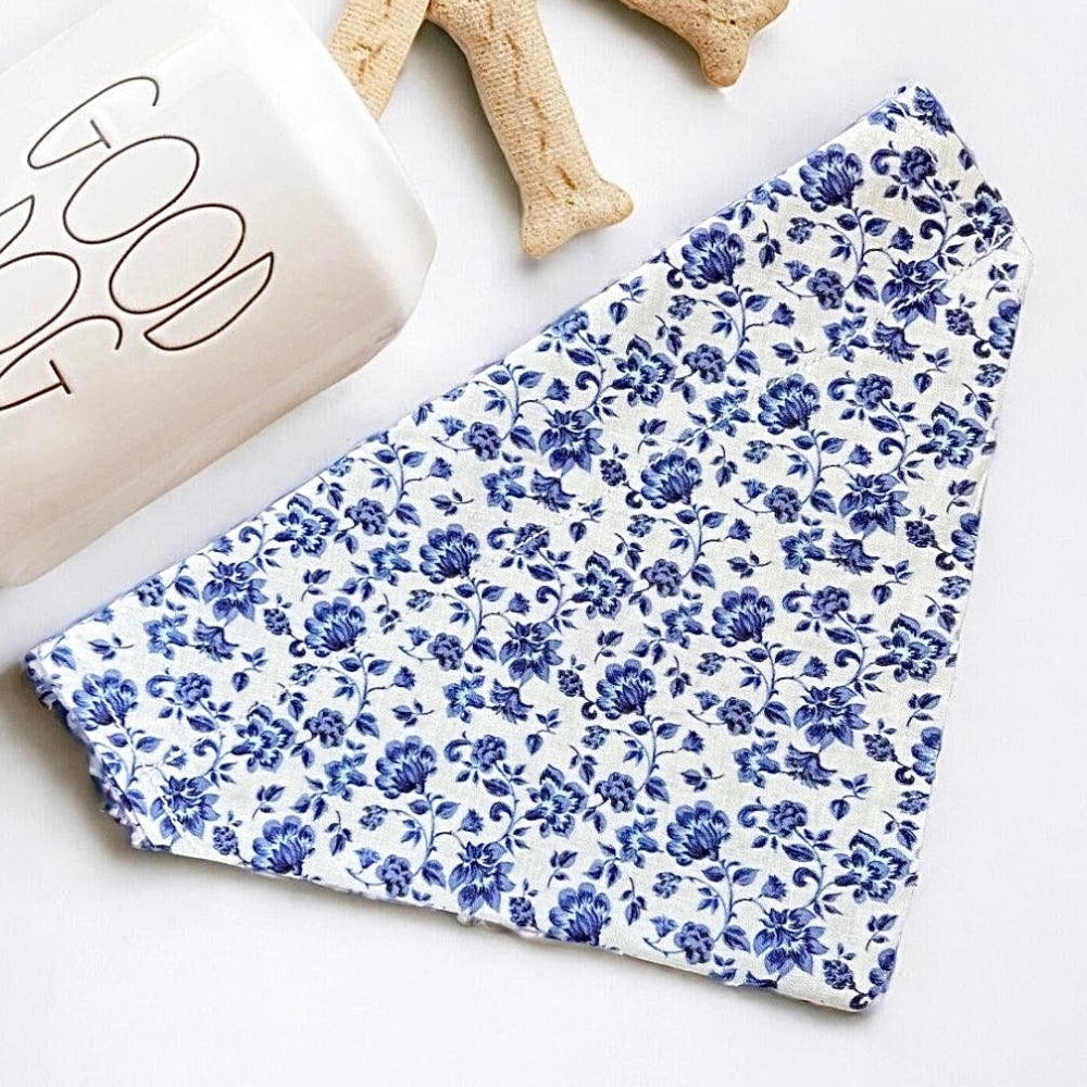 Blue floral dog bandana fabric on a white surface with a beige book and wooden object.