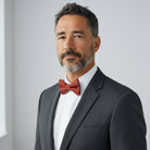 Man wearing a gray suit with a burnt orange bow tie against a light gray background