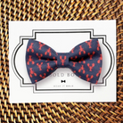 Navy blue dog bow tie with red lobster pattern on a card, placed on a woven surface.