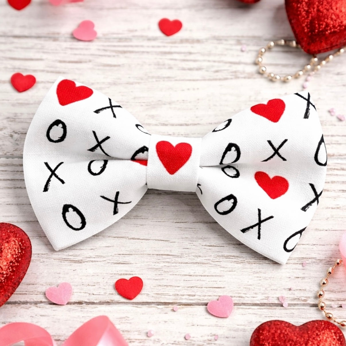 White Valentines Day bow tie with red hearts and black text on a wooden surface with heart decorations