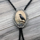 Raven Bolo tie with a black crow design on an oval pendant against a wooden background