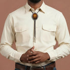 Infographic from The Bold Bow Tie titled Bolo Tie Features. Right: A vintage-style bolo tie with a blue and white cowboy riding a horse illustration inside an ornate bronze filigree frame on a black braided cord. Left: Lines connect the image to three checkmark features: Handmade, 39" Long Cord, and Pendant is 1.5" (L) x 1.25" (W). Bottom text reads Perfect Addition to Your Outfit.