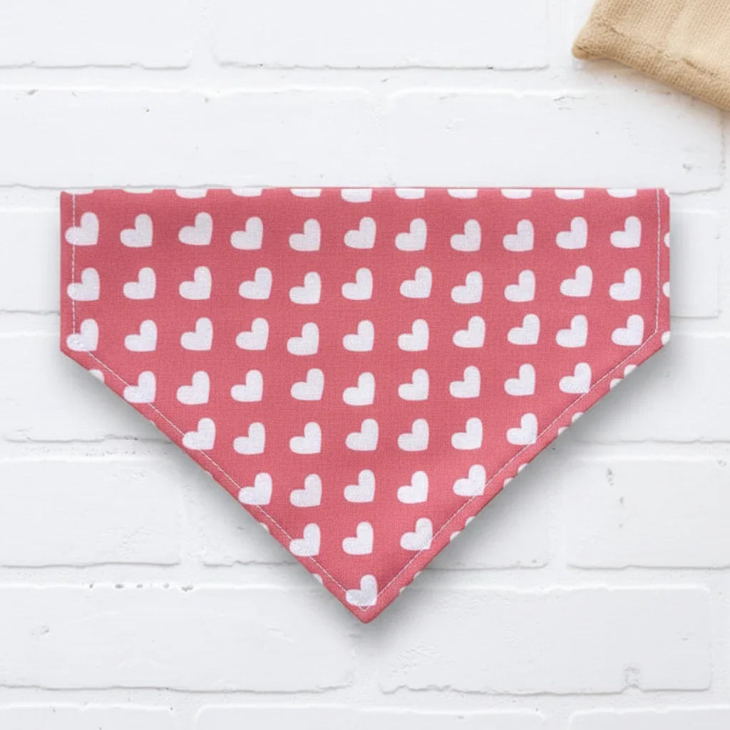 Pink Valentines Day dog bandana with white heart pattern next to a 'Good Dog' mug on a white surface
