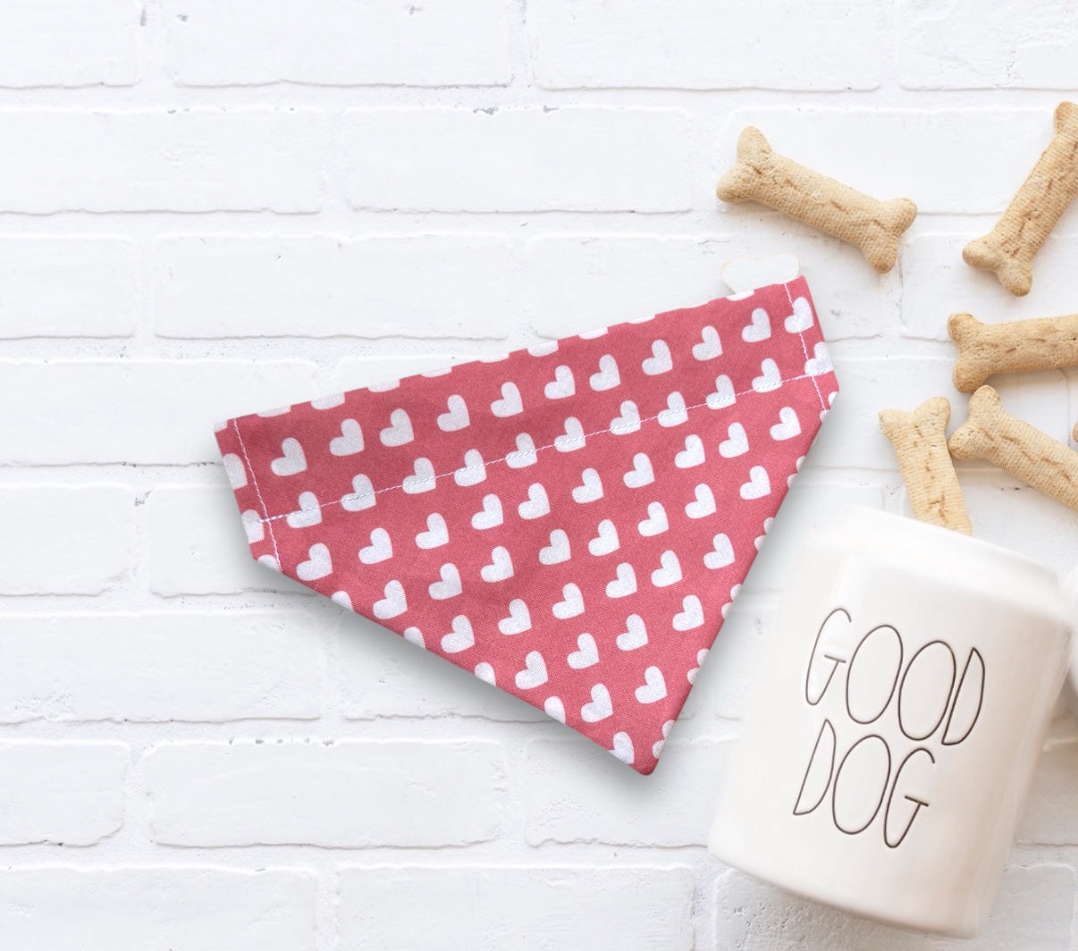 Pink Valentines Day dog bandana with white heart pattern next to a 'Good Dog' mug on a white surface