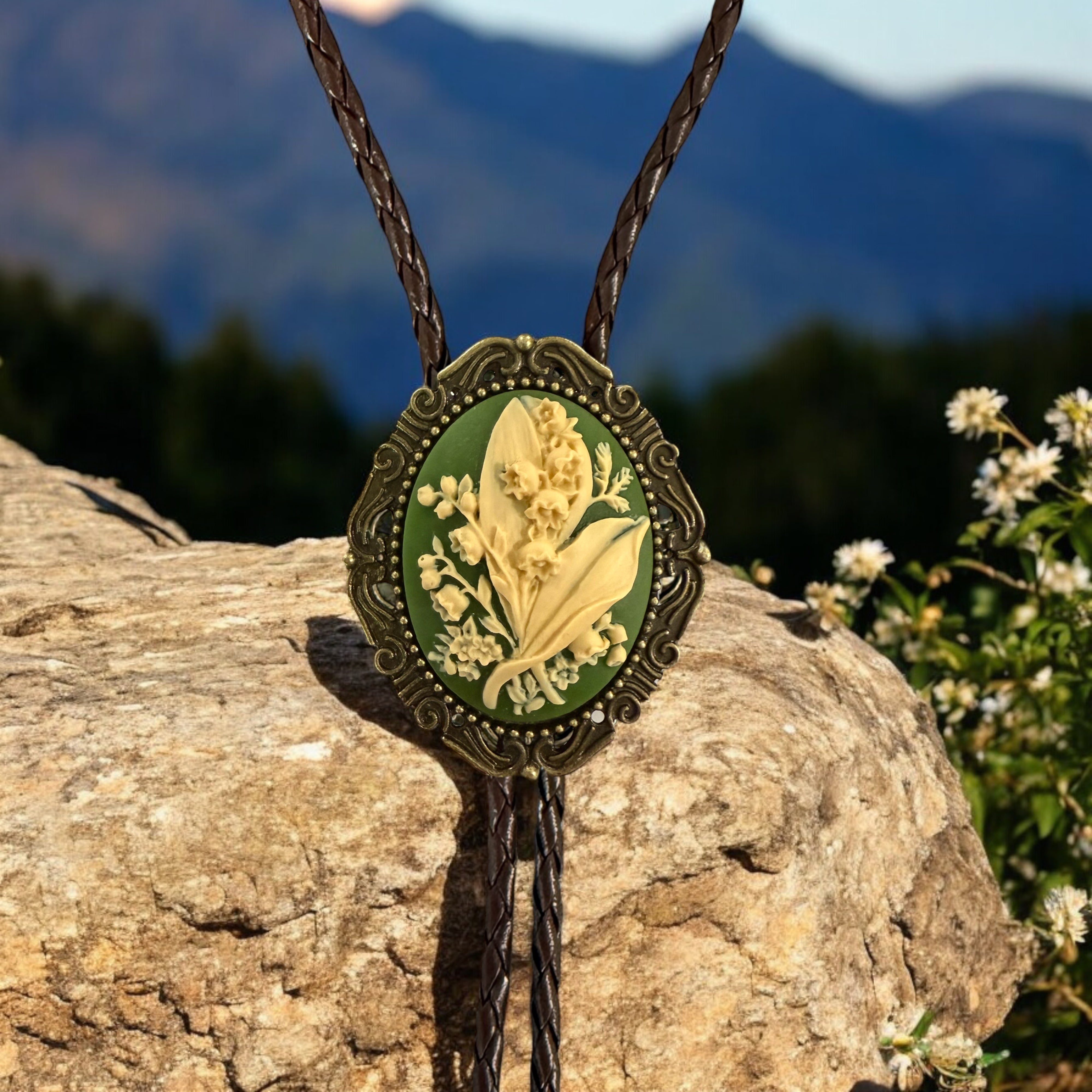 Decorative green lily of the valley with floral design bolo tie on a rock with mountain background