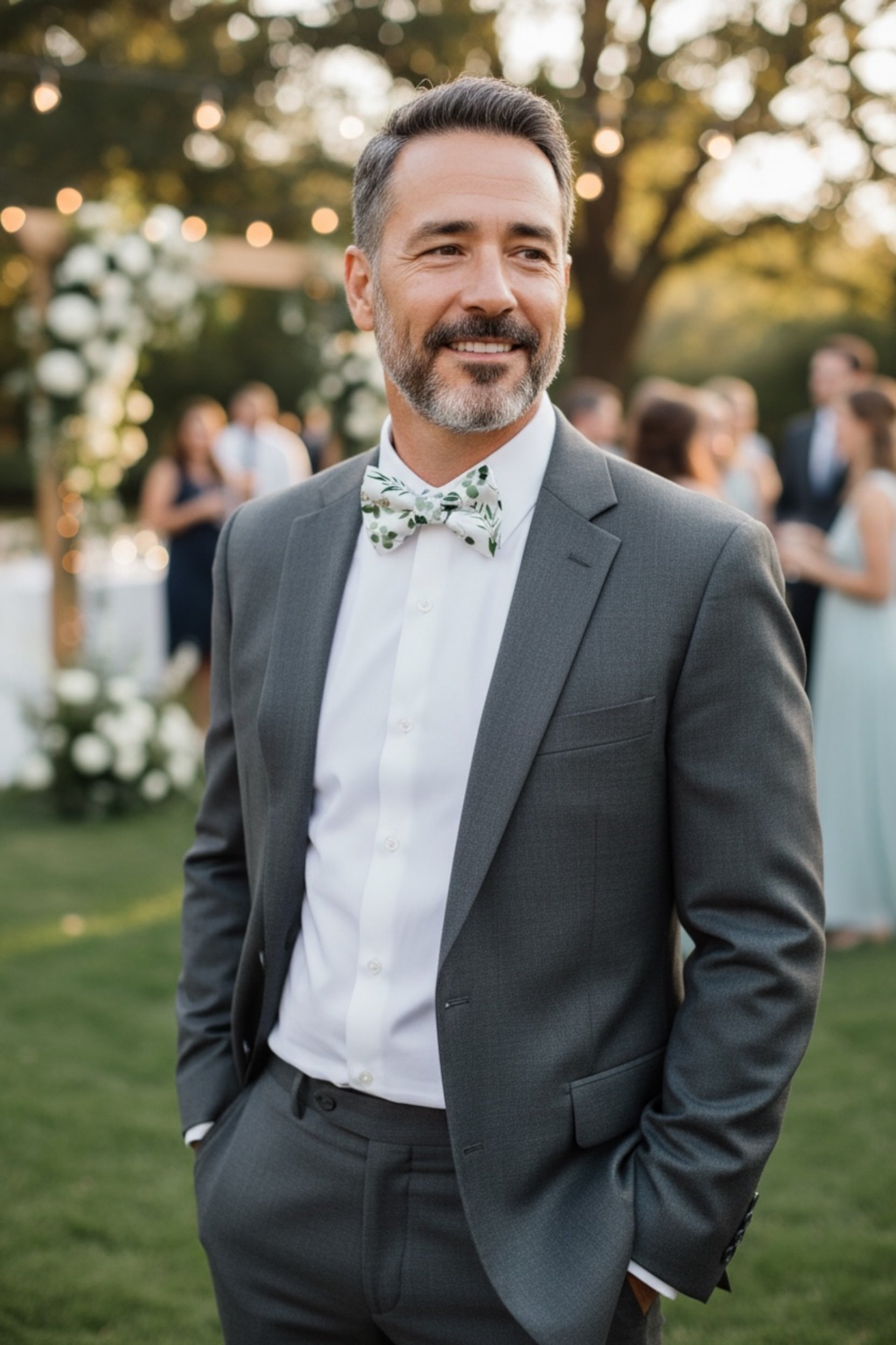 Groomsman in a gray suit with a dark green floral bow tie standing outdoors at a wedding.