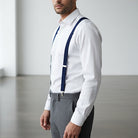 Man wearing navy suspenders for men, a white dress shirt, gray pants to be a groomsman in a wedding.