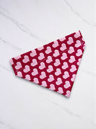 Red dog bandana with pink heart patterns on a white wooden surface