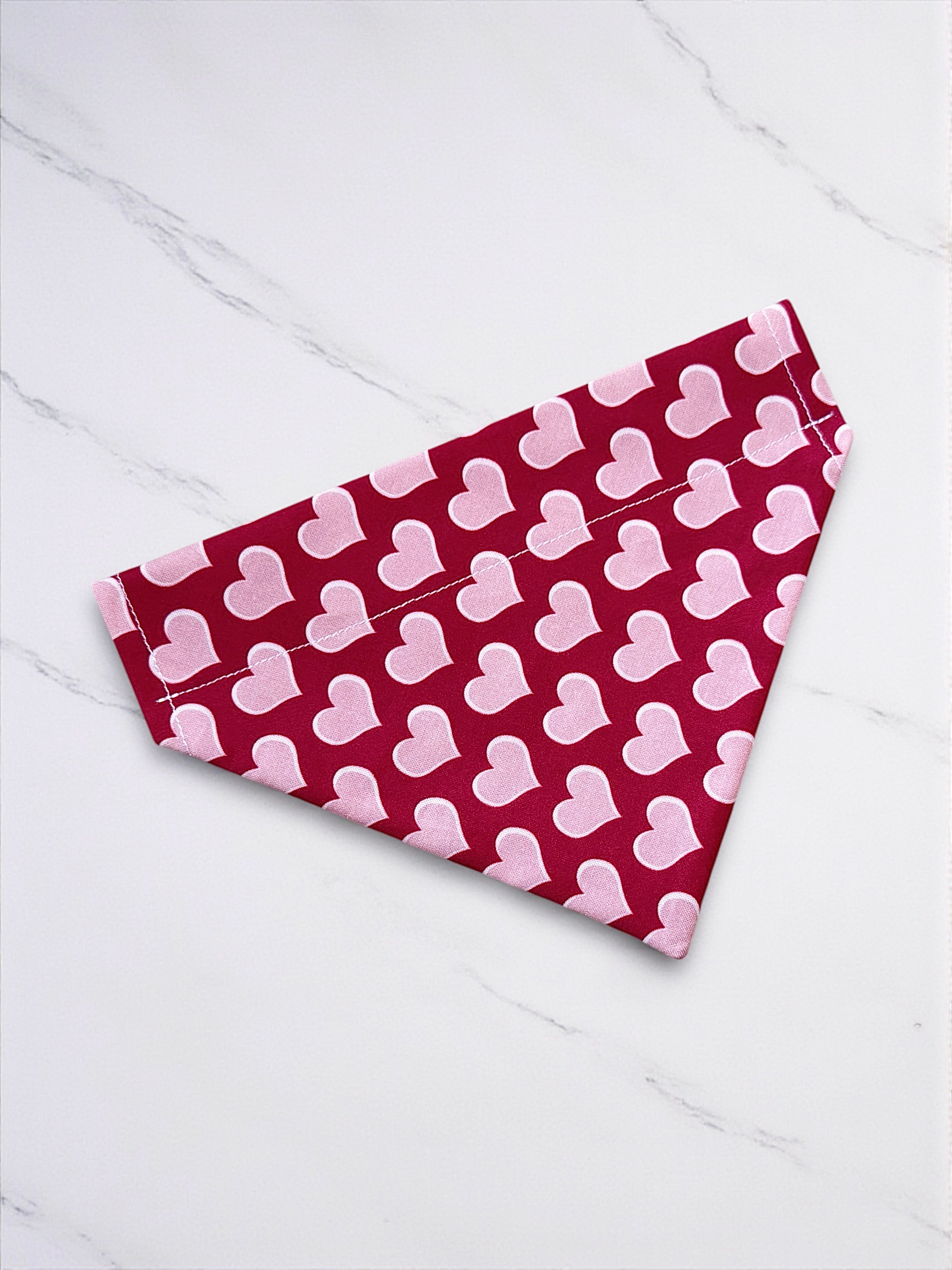 Red dog bandana with pink heart patterns on a white wooden surface