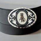 White gun raccoon belt buckle displayed on a black leather belt.