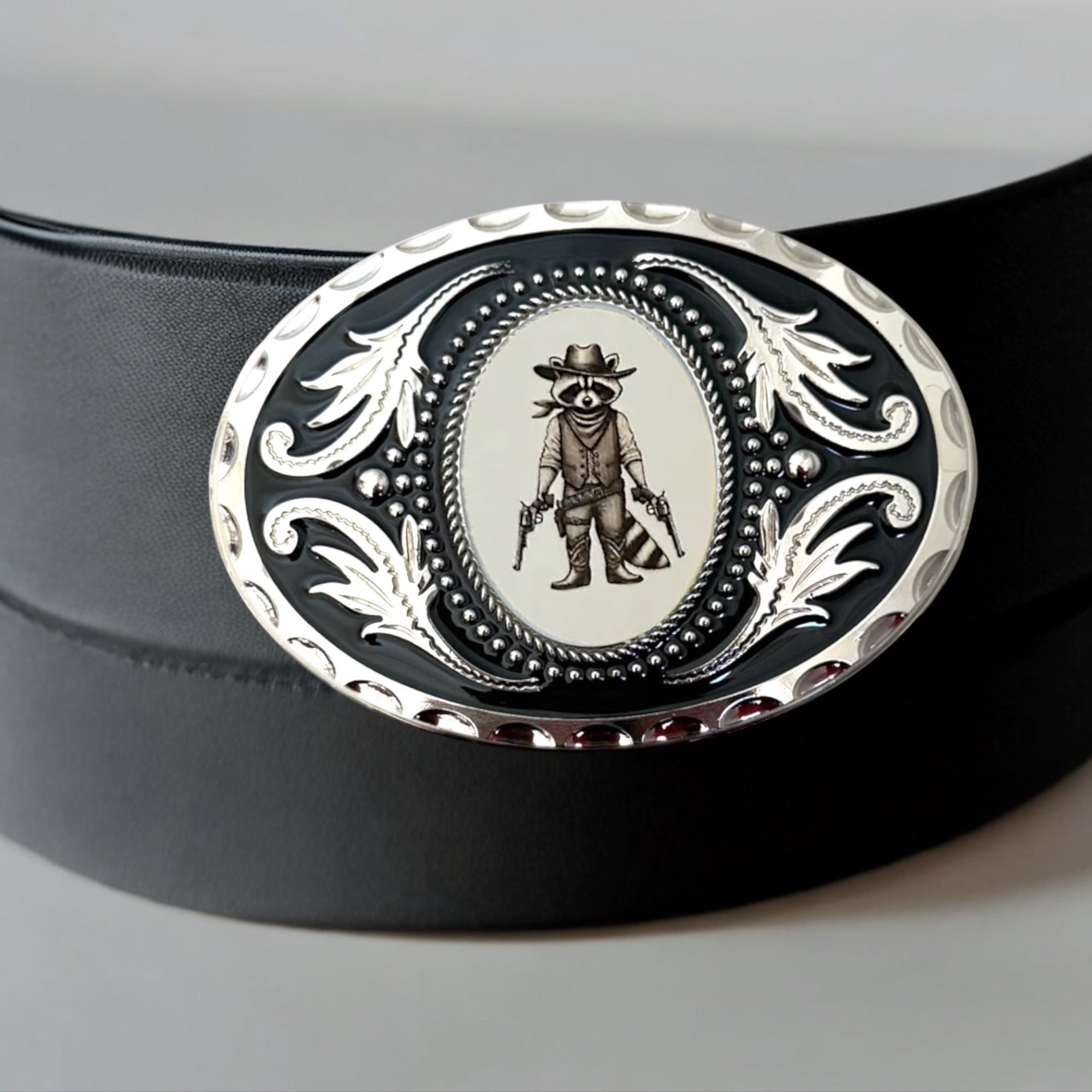 White gun raccoon belt buckle displayed on a black leather belt.