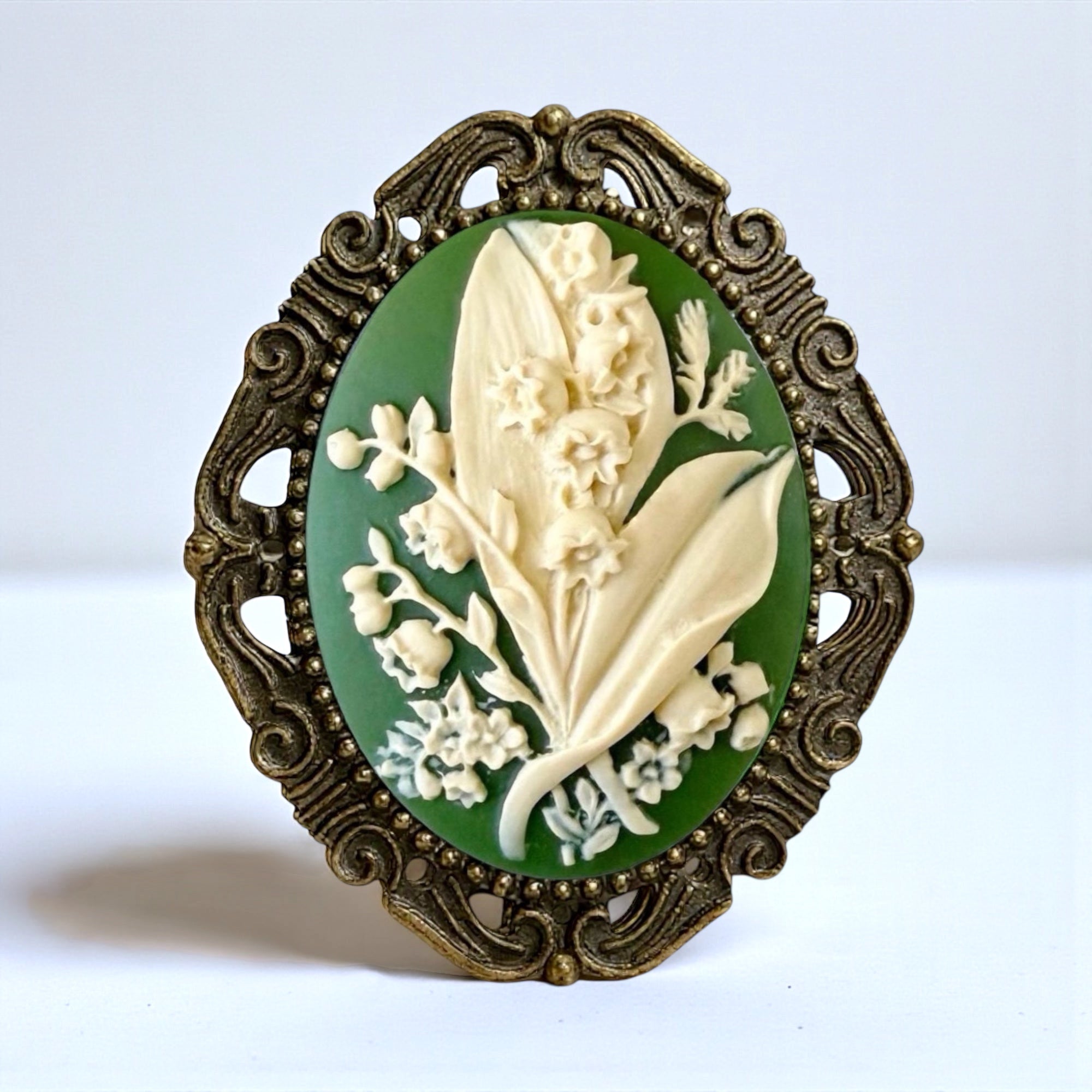 Decorative Vintage Style May Flower Green Lily of the Valley brooch with floral design and ornate bronze frame on a white background