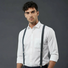 Groomsman wearing a white shirt and dark gray suspenders against a dark background