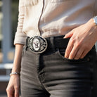 Person wearing a black belt with a decorative cat belt buckle, standing outdoors.
