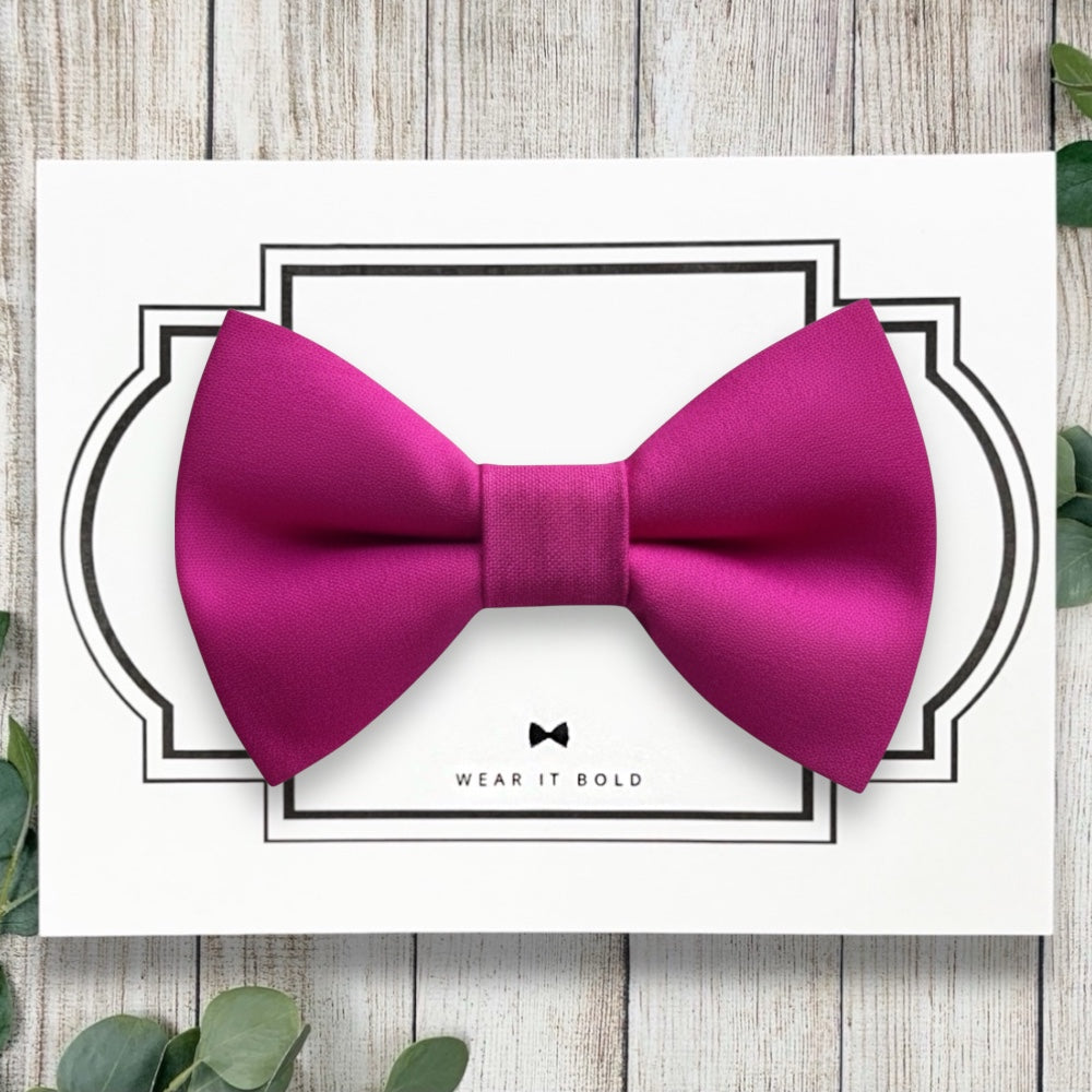 Pink dog bow tie on a white card with decorative border and 'Wear It Bold' text, placed on a wooden surface.