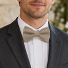 Close up of a groomsman in a taupe bow tie and suit for a wedding outfit.