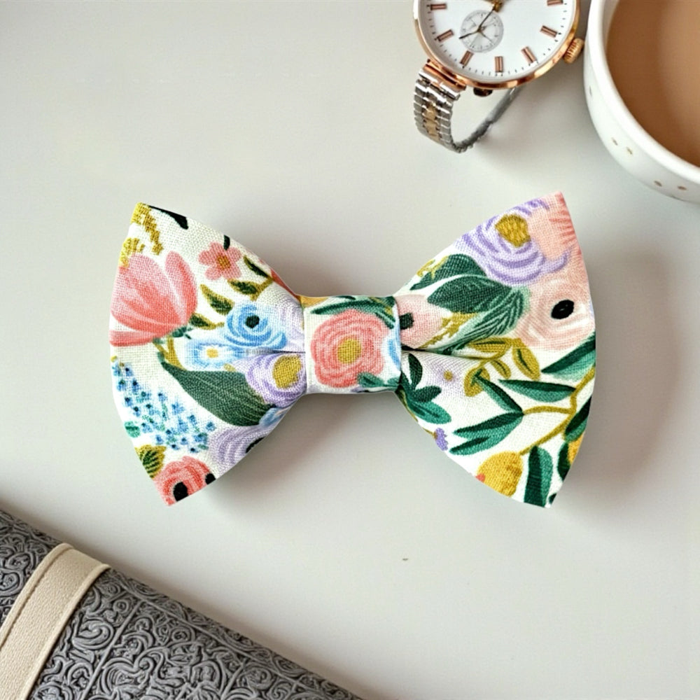 Floral bow tie on a white surface with a watch and cup of coffee in the background