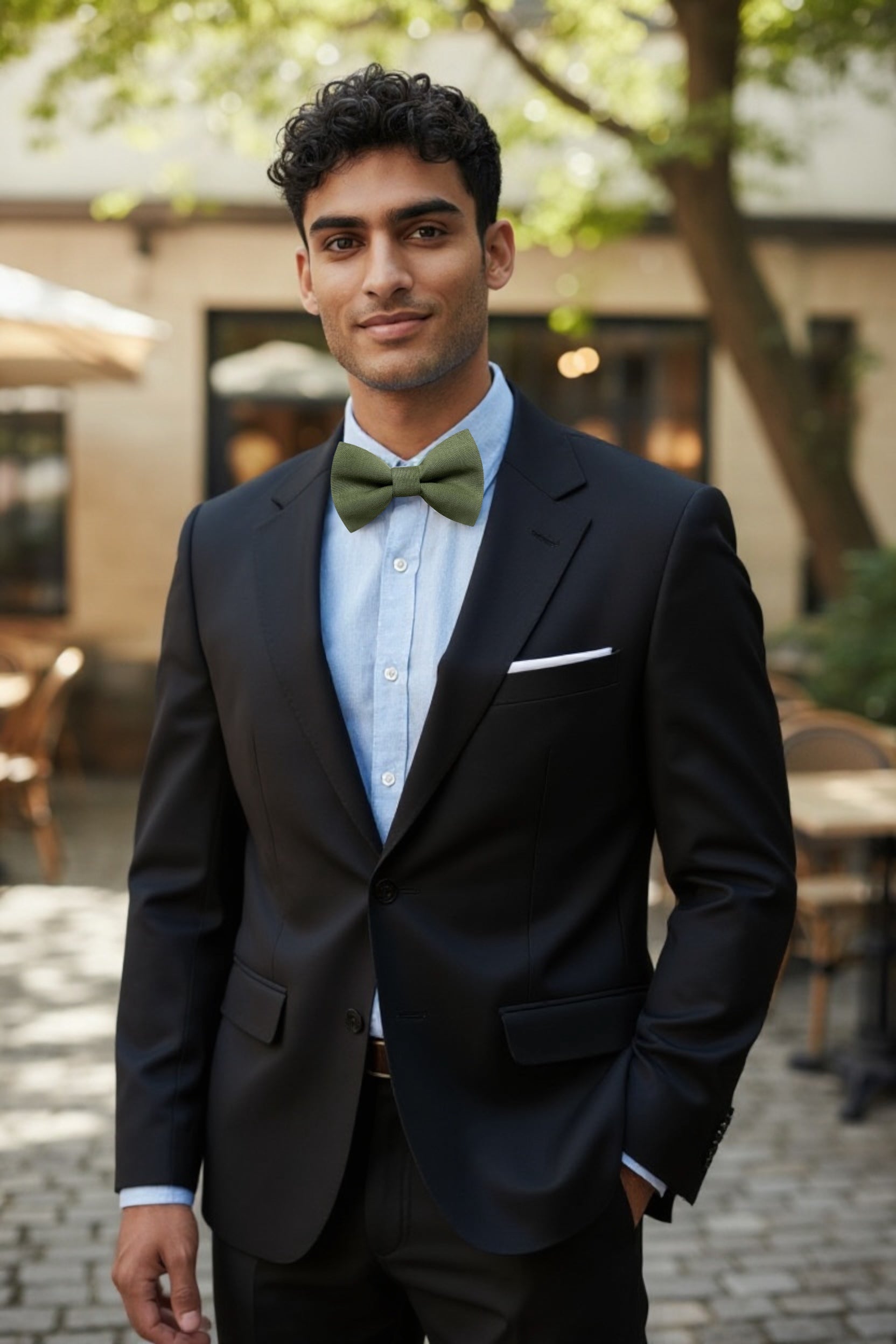 Groomsman in a black suit with an olive green bow tie standing outdoors.