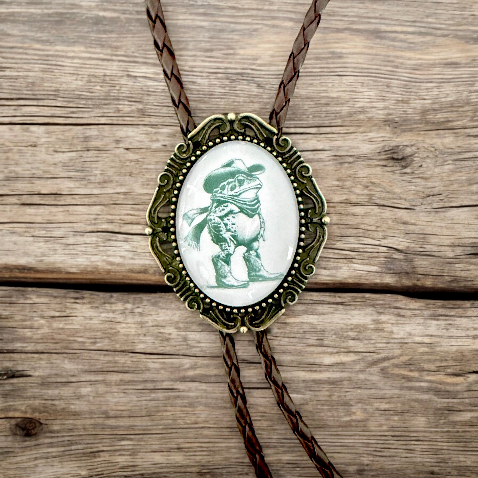 Bolo tie with a frog wearing a cowboy hat on a wooden surface