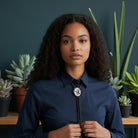 Woman wearing a blue shirt with a cat bolo tie in front of potted plants