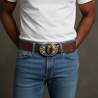 Person wearing blue jeans with a brown belt and large Tiger’s eye buckle against a neutral background