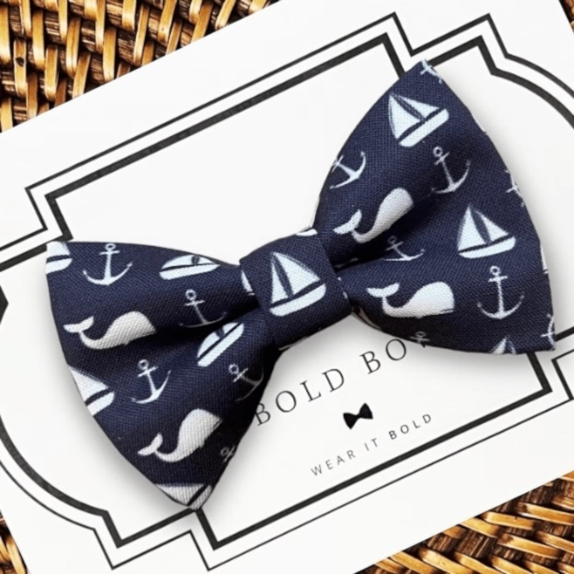 Navy blue dog bow tie with white sailboat and anchor pattern on a Bold Bow branded card.