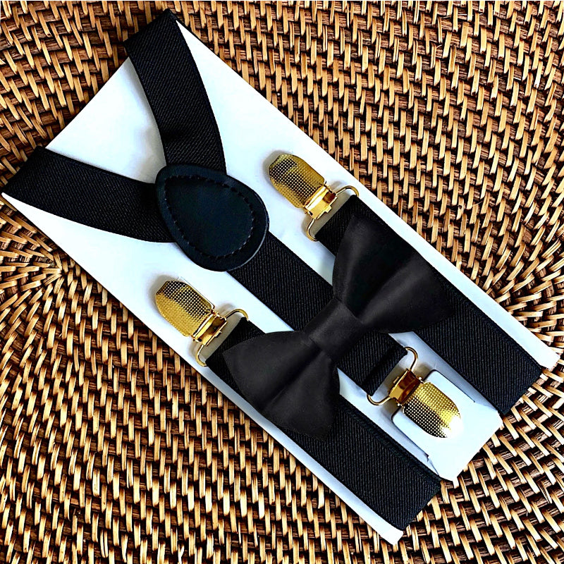 Black bow tie and suspenders with gold clasps on a woven surface