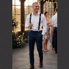 Groomsman in suspenders and a white shirt walking through the reception at an elegant wedding.