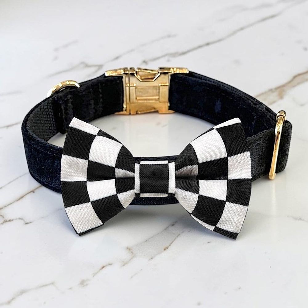 Black velvet dog collar with black and white checkered pt bowtie a gold clasp on a marble surface.