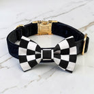 Black velvet dog collar with black and white checkered pt bowtie a gold clasp on a marble surface.