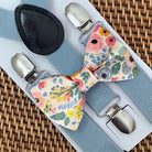 Floral bow tie with silver clips on a woven surface for groomsmen and ring bearers in weddings.