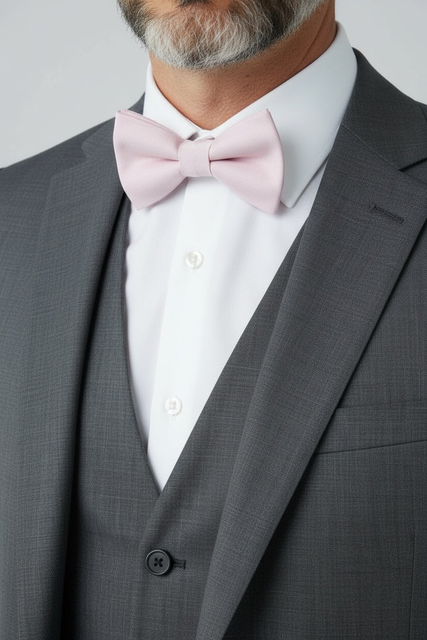 Groomsman in a gray suit with a light blush pink bowtie with a white shirt on a plain background