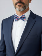 Groomsman wearing a navy floral bow tie in a wedding with a white shirt and suit against a plain background