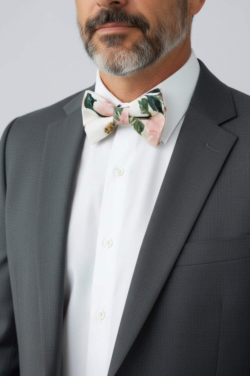 Groomsman wearing a gray suit with a white shirt and white and pink floral bow tie against a light gray background