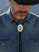 Cowboy wearing an opossum bolo tie for men wearing a denim shirt with a decorative bolo tie against a blurred natural background
