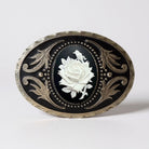 Decorative silver belt buckle with a white rose design on a black background in a studio setting