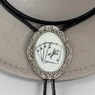 Silver cards bolo tie with playing card design on a beige cowboy hat.