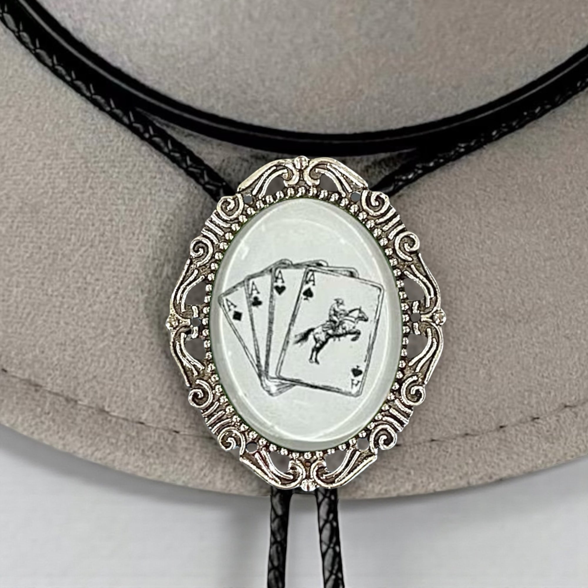 Silver cards bolo tie with playing card design on a beige cowboy hat.